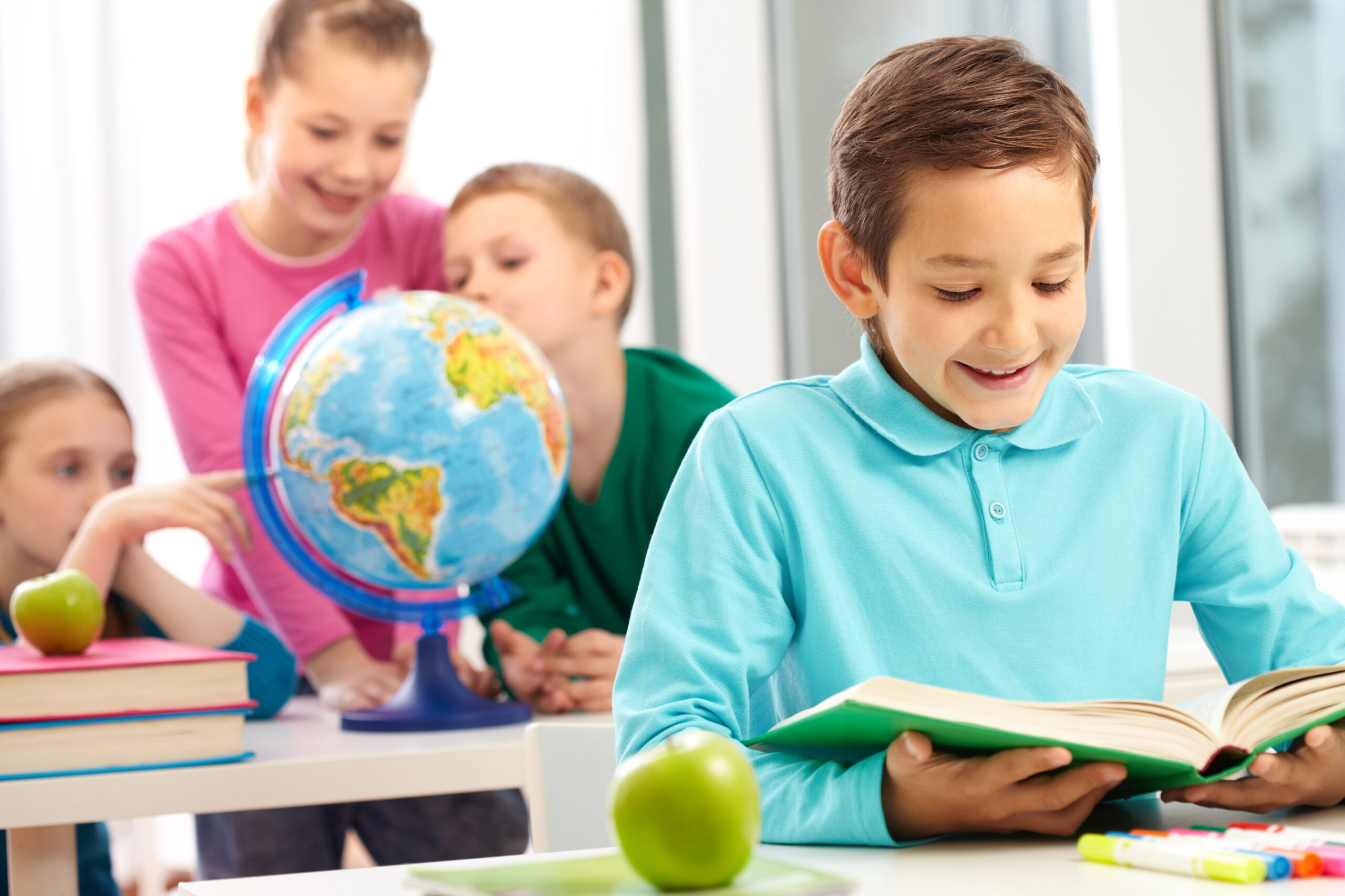 Cute schoolboy reading book in class on background of classmates